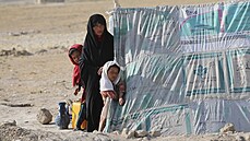 Afghánská žena stojí se svými dcerami před provizorním stanem v uprchlickém... Afghánská žena stojí se svými dcerami před provizorním stanem v uprchlickém...
