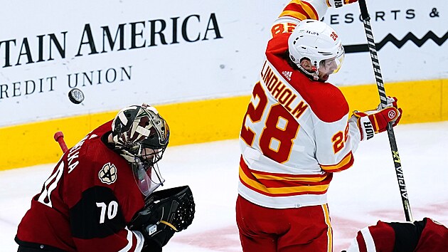 Brankář Arizony Karel Vejmelka musí reagovat na teč Eliase Lindholma z Calgary.