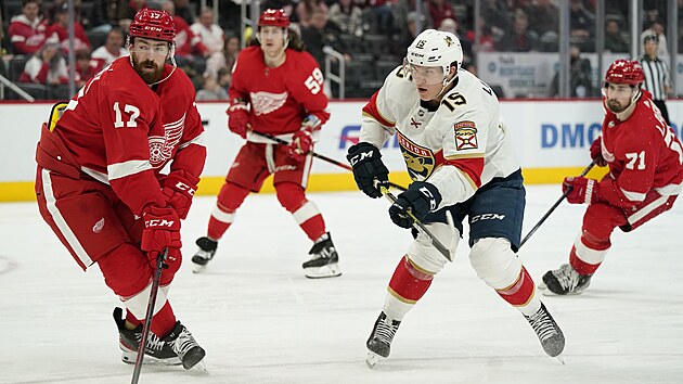 Filip Hronek (vlevo) z Detroitu se ohlíží za pukem, který vyslal centr Floridy Anton Lundell (uprostřed)