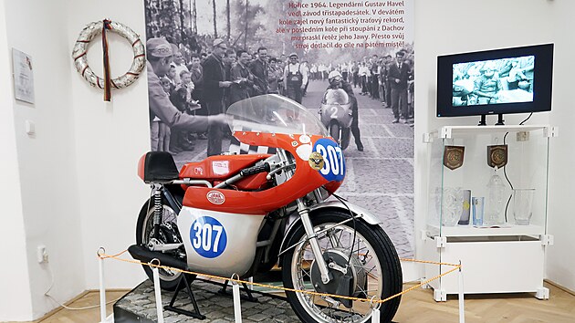 Gustav Havel vedl v roce 1964 v zvod tistapadestek v Hoicch, ale v poslednm kole mu praskl etz. Motocykl dotlail do cle a skonil pt, ukazuje fotografie v pozad hoick expozice.