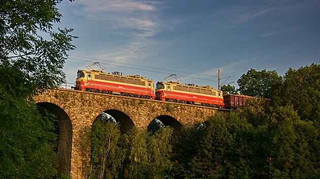 Dvojice retro laminátek 230.091 a 230.061 v polomáčeném nátěru v čele průběžného nákladního vlaku dopravce ČD Cargo. Krátce před západem slunce vlak opustil stanici Jihlava město a po kamenném viaduktu míří vstříc stanici Jihlava. Fotografie byla pořízena krátce před půl devátou večer dne 20. července 2022.