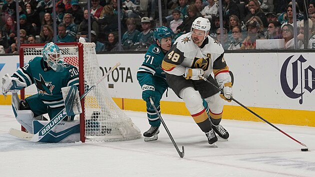 Tomáš Hertl hledá cestu zpoza brány, brání ho Macklin Celebrini, situaci sleduje brankář Jaroslav Askarov.