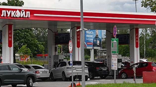 Lidé čekají ve frontě na tankování u čerpací stanice Lukoil v ruském Petrohradu. V pozadí stojí billboard s nápisem „Pýcha Ruska“ věnovaný účastníkovi války proti Ukrajině. (7. července 2026)