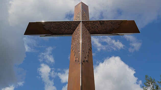 Bronzov&aacute; ka&scaron;na, symbolizuj&iacute;c&iacute; křtitelnici, a bronzov&yacute; kř&iacute;ž, připom&iacute;naj&iacute;c&iacute; konec životn&iacute; pouti, je propojen kamennou řekou života. (27. července 2026)