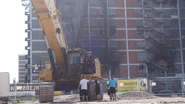 Přípravy na demolici vyhořelé budovy 34 finišují. Klíčovým strojem bude obří demoliční bagr Caterpillar o provozní hmotnosti kolem 100 tun, jeden z největších demoličních strojů na světě. (srpen 2026)