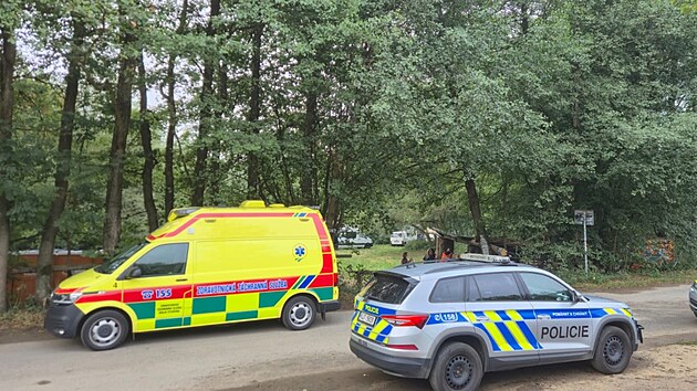 Dvojice vozidel IZS u vjezdu do lokality. Tento záběr dokumentuje trvalou přítomnost zdravotníků i policistů na místě.
