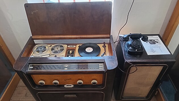 Vlevo stoj&iacute; masivn&iacute; radiogramofon značky Tesla, kter&yacute; v jedn&eacute; skř&iacute;ni sdružuje r&aacute;dio, gramofon i c&iacute;vkov&yacute; magnetofon. Aby byl poslech hudby plnohodnotn&yacute;, doplňuje jej samostatn&aacute; reproduktorov&aacute; skř&iacute;ň vpravo.