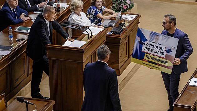 Premiér Andrej Babiš hovoří na mimořádné schůzi Sněmovny před hlasováním o nedůvěře vládě. Lidovec Marian Jurečka si před něj stoupl s plakátem, v němž lidovci Babišovi vyčítají návrh schodku rozpočtu na příští rok 386 miliard korun. (29. září 2026)