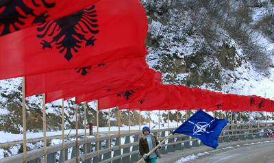 Kosovský Albánec nese vlajku NATO na most, který je vyzdoben albánskými vlajkami.