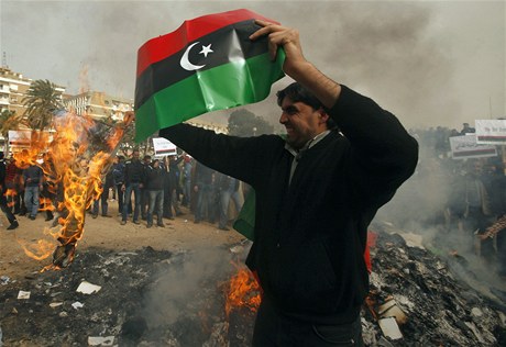 Demonstrant v Benghází s libyjskou vlajkou. V pozadí protestující pálí Kaddáfího Zelenou knihu.