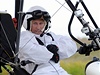 Pilot deltaplánu v bílém odní, napodobujícím vzhled dosplého jeába, v roli 
