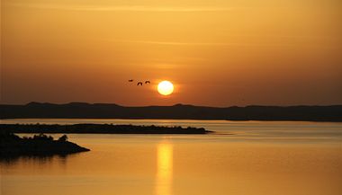 Kovit pohled na jezero, pamtku a vychzejc slunce, skrz kter proltv hejno ptk