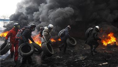 Demonstranti vytvej barikdu z hocch pneumatik. Ped kouem se chrn roukou.