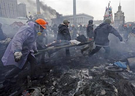 Demonstranti na Majdanu se pokouejí penést zranného druha do bezpeí.