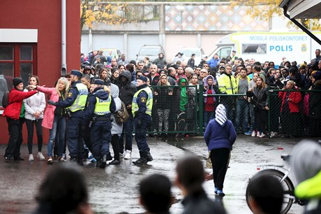 Policisté udrují dav pihlíejících lidí mimo ohrazený areál.