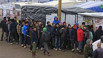Migranti v tboe v Calais stoj frontu na distribuovan obleen.