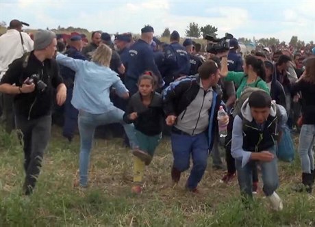 Maarská kameramanka (v modrém) podráí nohy mladé migrantce.