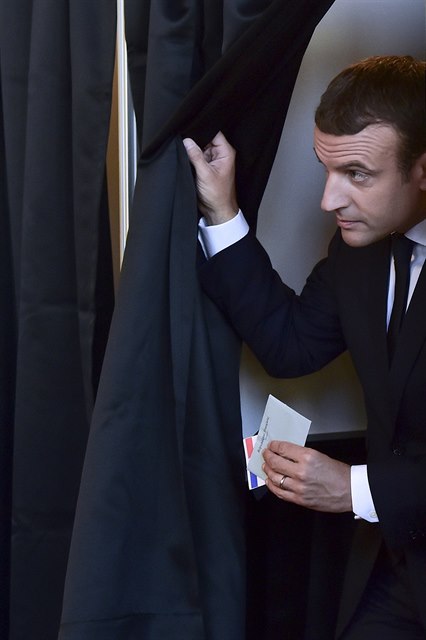 Francouzský prezident Emmanuel Macron vychází zpoza plenty se svým hlasovacím...