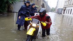 Policisté pomáhají mu vést motorku zatopenou ulicí.