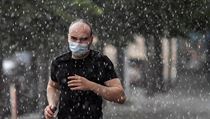 Muž v ochranné roušce proti šíření koronaviru běží za přívalového deště při...