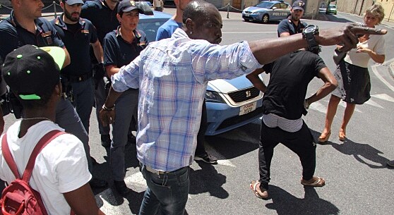 Protest migrant v Prato. Migrant vytahuje ped jednou enou mobil z trenek ...