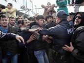 Strkanice mezi eckými policisty a migranty v uprchlickém táboe v Athénách.