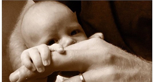 Malý Archie nn drí prst táty Harryho.