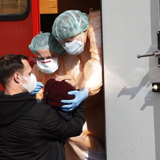 Medical staff members wearing protective suits take samples from a young boy to...