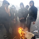 Nohy si migranti ohřívají nad ohněm.