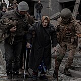 Vojáci pomáhají stařence při přechodu zničeného mostu na okraji Kyjeva.