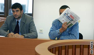 Odsouzený Jan Hudák se kryje novinami u plzeského soudu.