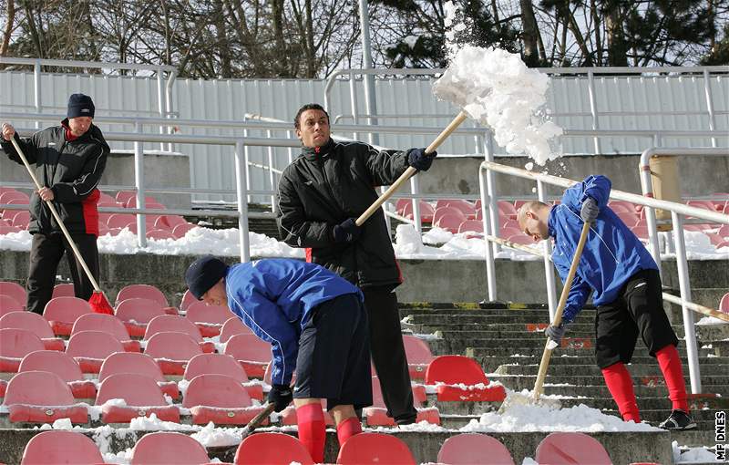 Fotbalisté 1. FC Brno uklízí sníh ze sedaek stadionu na Srbské