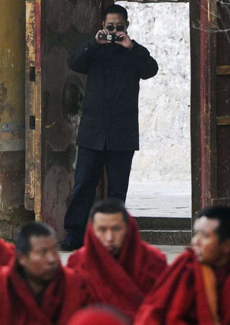 Tibetsk mnichy na kadm kroku hldaj policist v civilu (na pozad)