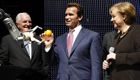 Robot Marvin podává Arnoldu Schwarzeneggerovi pomeranč, vpravo přihlíží německá kancléřka Angela Merkelová (vlevo je šéf firmy Intel) 