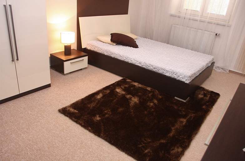 Svtlý celoploný koberec vedle postele dopluje tmav hndý kusový, který je sladn s rámem postele ze deva wengé