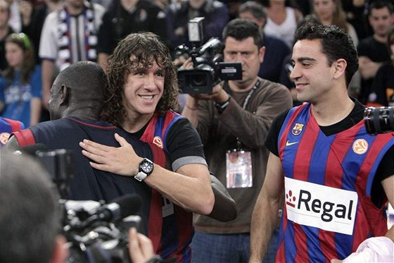 Kapitán fotbalové Barcelony Carles Puyol gratuluje k euroligovému triumfu basketbalistovi Bonifaci N´Dongovi. Vpravo pihlíí Xavi