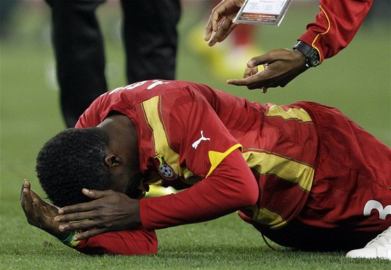 JÁ ZA TO MَU. Ghanský útoník Gyan padá na trávník, v rozhodující moment nedal penaltu.
