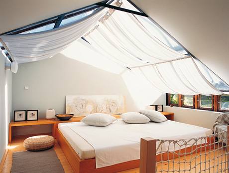 Hostinský pokoj s impozantní postelí, nad níž se vyjímá lněný zastiňovací závěs