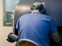Pan primář sedící u přístroje, hledí do 3D prostoru těla pacientky, joysticky a pedály ovládá operační nástroje na dálku.