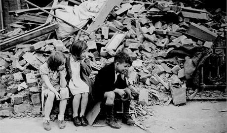 Děti z východního předměstí Londýna sedí u vybombardovaných trosek domu, kde předtím bydleli. (1940)