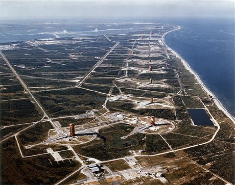Letecký pohled na řadu ramp vojenské části kosmodromu Cape Canaveral; civilní část Kennedy Space Center je vzadu na obzoru