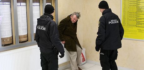 Bezdomovce ohívajícího se u topení v hale libereckého nádraí kontroluje hlídka mstské policie.