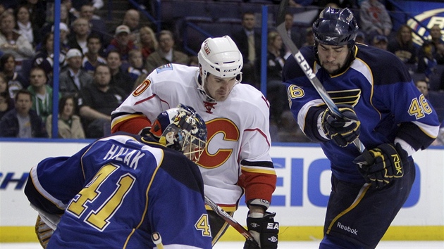 MEZI POLÁKEM A HALÁKEM. Curtis Glencross (v bílém) z Calgary se snaí pekonat slovanského brankáe St. Louis Jaroslava Haláka. Brání ho eský bek Roman Polák.