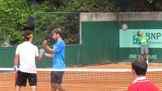 Zatímco Ryan Harrison (v modrém) gratuluje svému soupe�i k postupu, mladý sb�ra� mí�k� (vpravo) sleduje let Ameri�anovy rakety mezi v�tve strom�