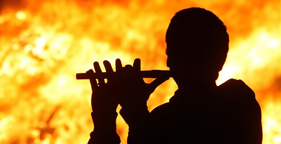 Njaký mu hraje na flétnu ped hoící hranicí, kterou zapálili protestanti