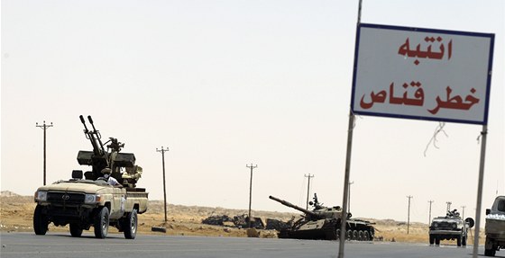 Libyjtí povstalci projídí kolem znieného tanku Kaddáfího jednotek.