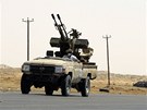 Libyjtí povstalci projídí kolem znieného tanku Kaddáfího jednotek.