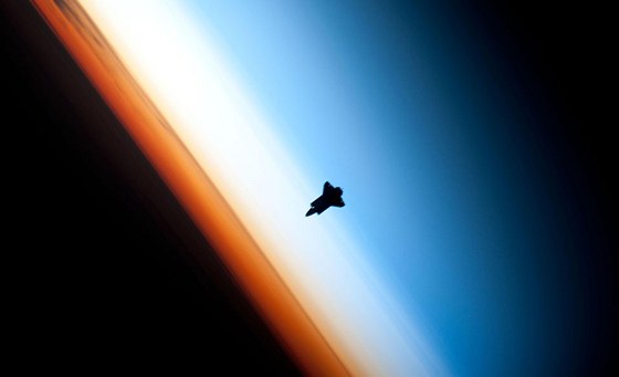 Silueta raketoplánu Endeavour nad zemským obzorem na snímku z Mezinárodní vesmírné stanice