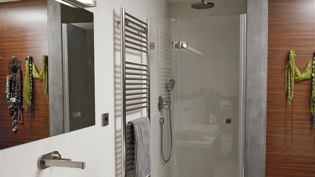 Jednoduchou koupelnu v šedobílé kombinaci doplněné tmavou dýhou zdobí matné