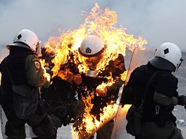 etí policisté pomáhají svému kolegovi, který vzplál po zásahu molotovovým...